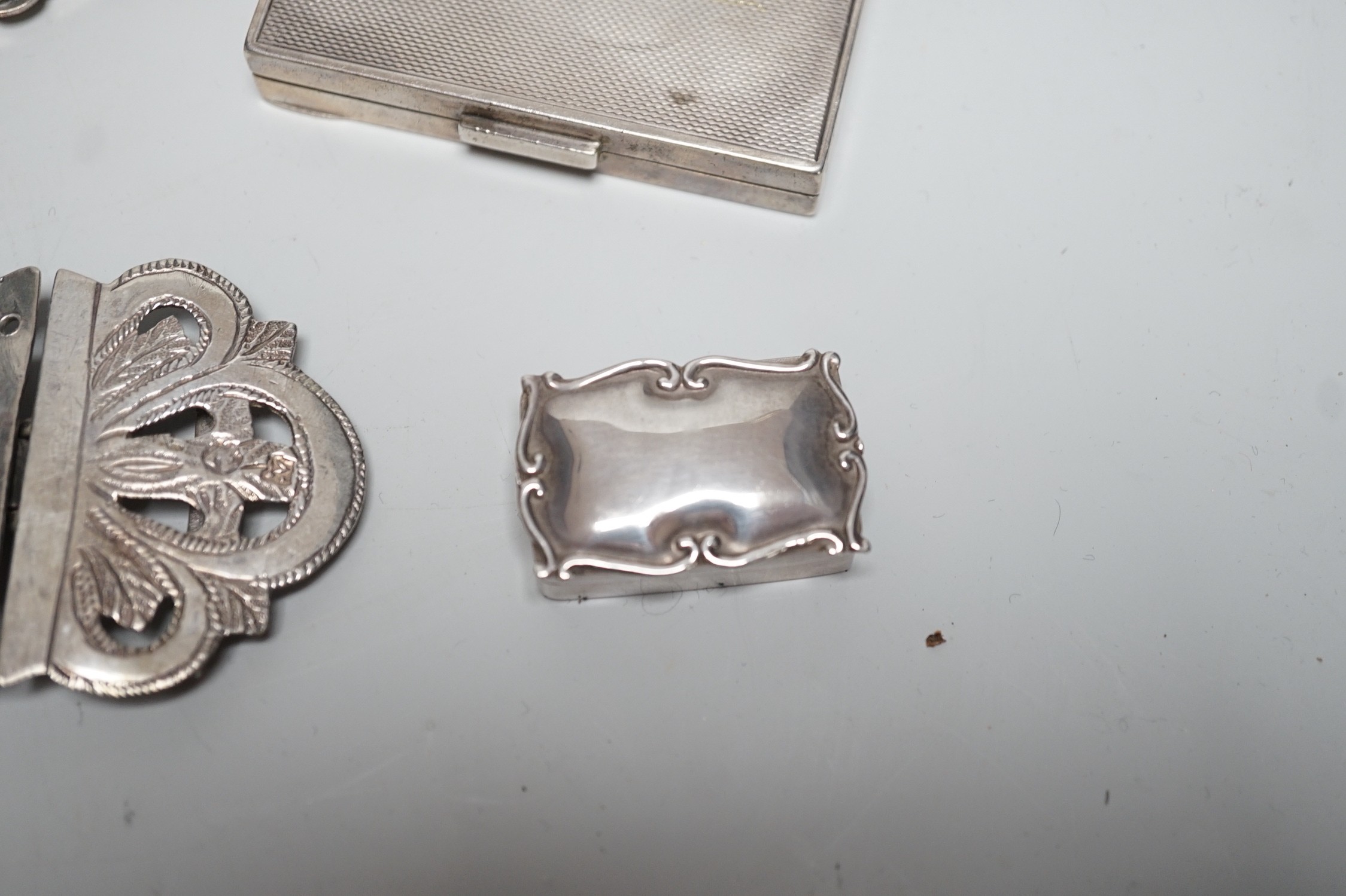 A George VI engine turned silver compact, 69mm, two modern silver pill boxes, a Persian white metal belt buckle, a silver vesta case and a base metal compact.